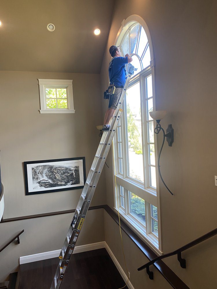 Image of a Capt. Clean employee standing on a ladder cleaning a customer's interior windows.