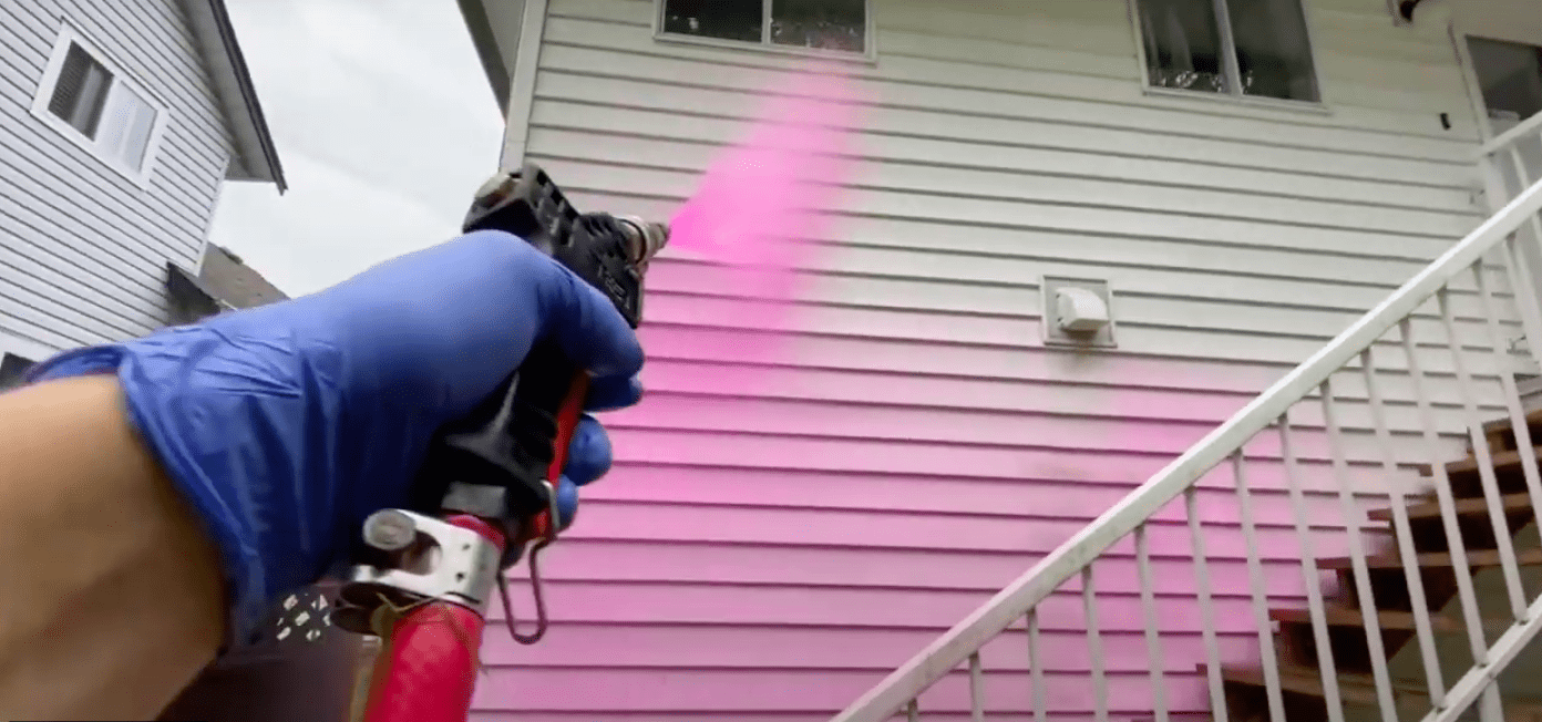 Image of technician spraying a pink soap on the side of a house.