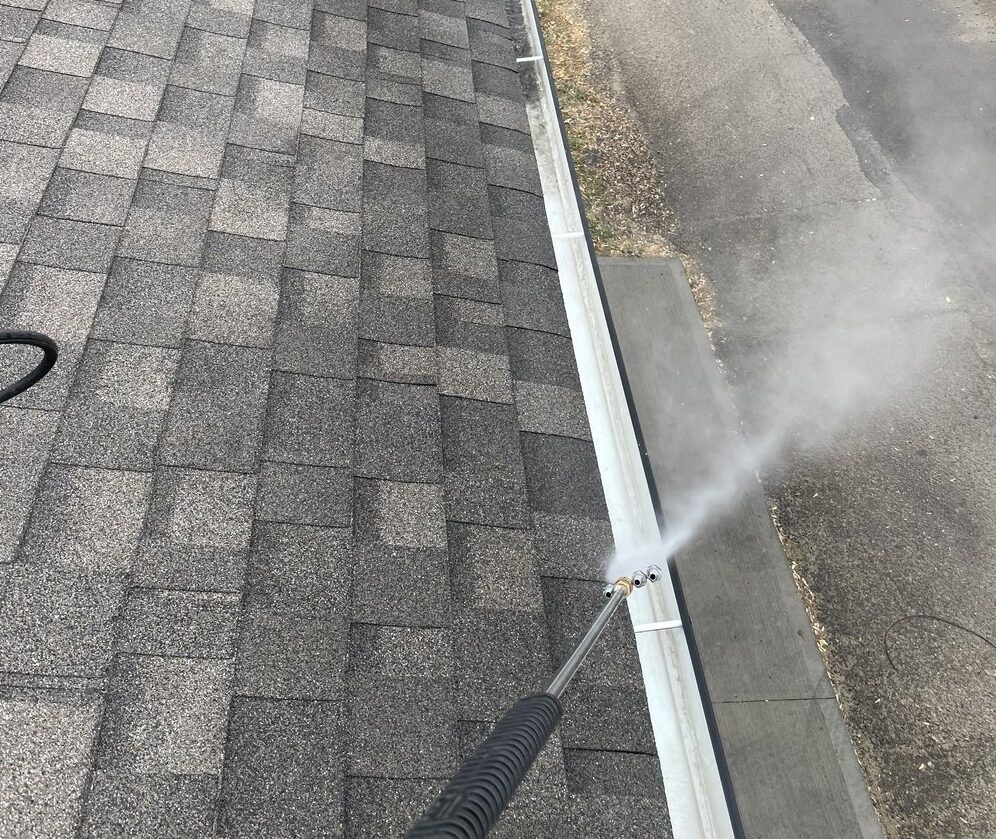 Image of power washing wand spraying water to clean out roof gutters on a residential home.