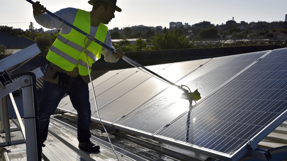 Image of a worker cleaning a solar panel in the sun.